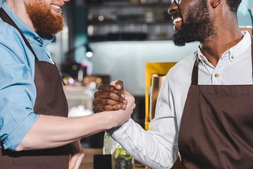 cropped image of two smiling owners of coffee shop shaking hands