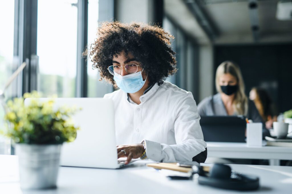 Portrait of young man with face mask back at work in office after lockdown.