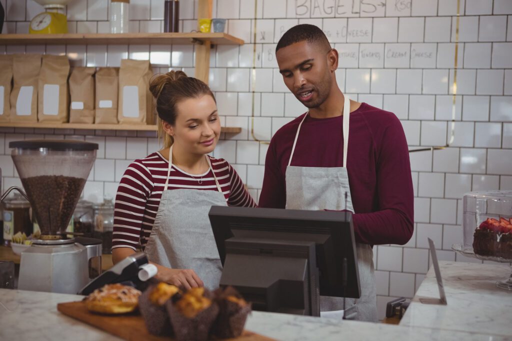 Young owners using cash register while standing in cafe