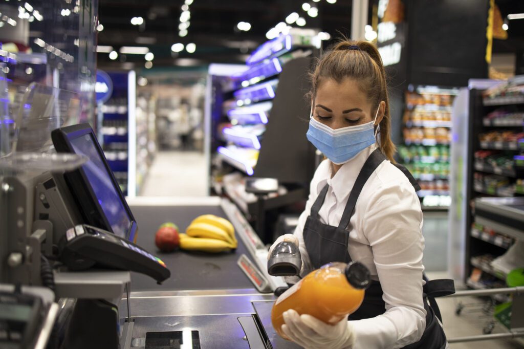 Cashier in supermarket wearing mask and gloves fully protected against corona virus. Working during covid-19 pandemic.