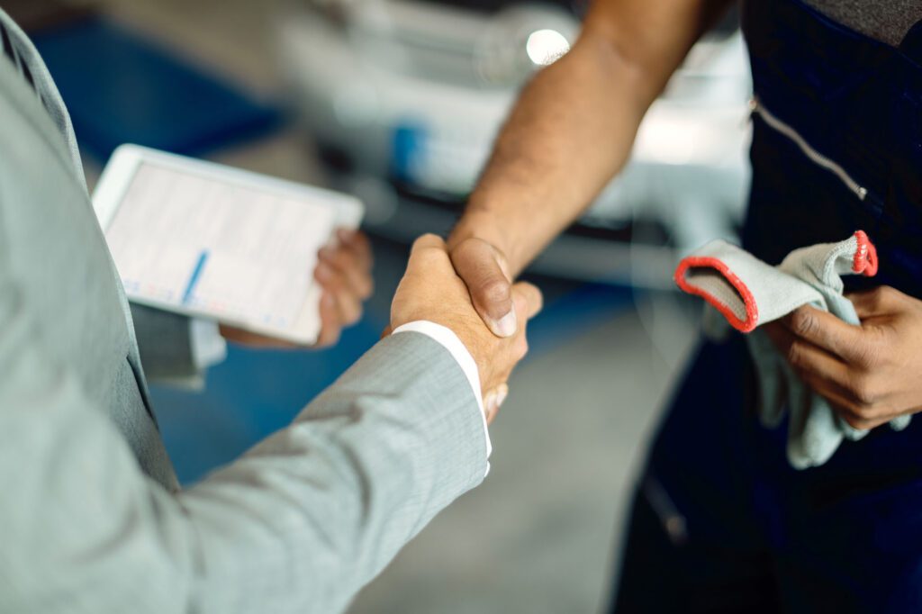 Close-up of businessman handshaking with auto mechanic in a workshop.