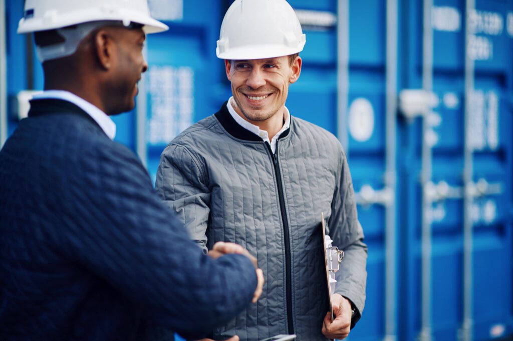 Smiling engineers standing in a shipping yard shaking hands together