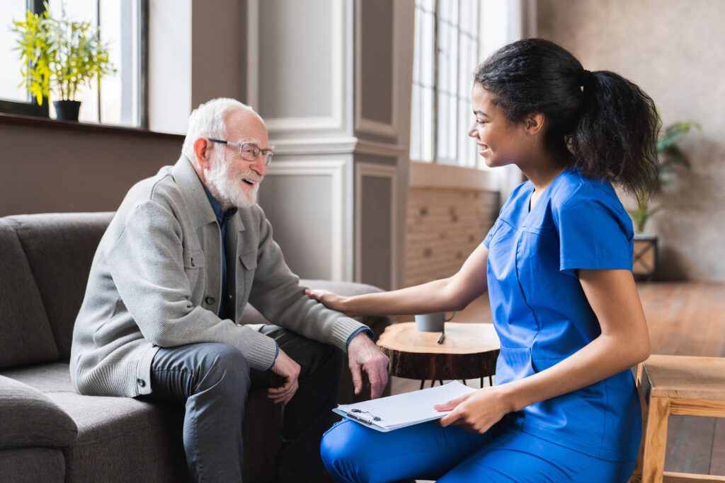 African nurse in uniform talking during day visit to old patient grandfather. Caring caregiver hold hand of 80s senior elderly man people having pleasant conversation, satisfied grandfather receiving support and care from carer concept