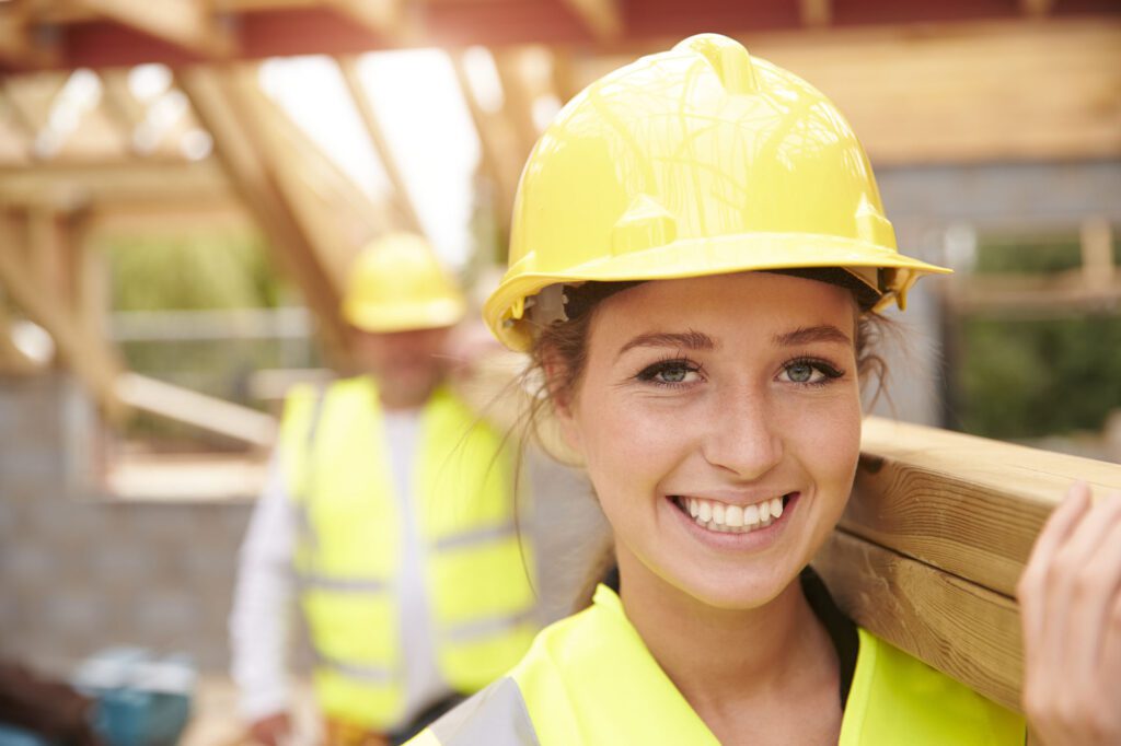 Builder And Female Apprentice Carrying Wood On Site