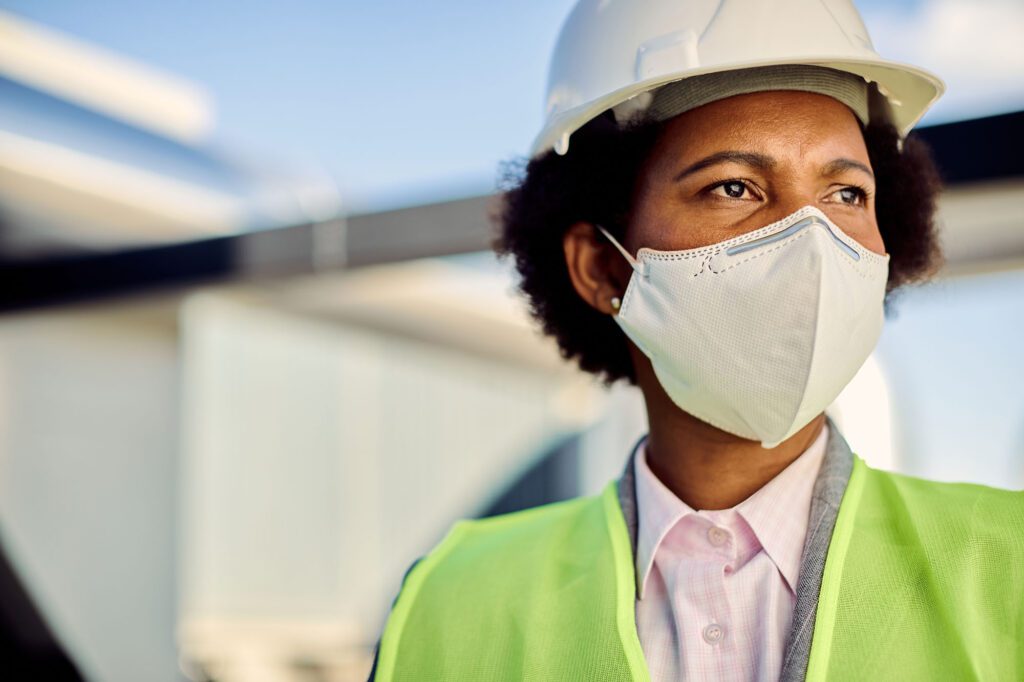 Female African American civil engineer with protective face mask at construction site.