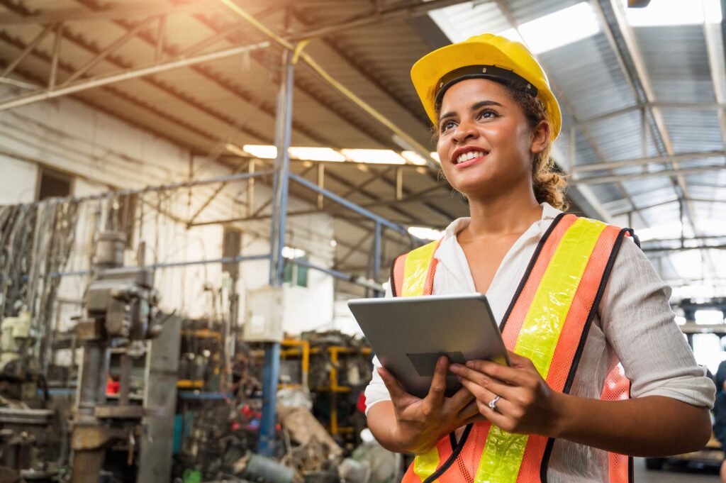 Female industrial worker working and checking machine in a large industrial factory with many equipment.