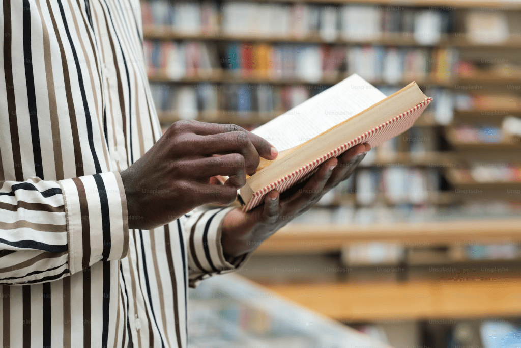 Close-up of an open book held in the hands of someone wearing a striped shirt.