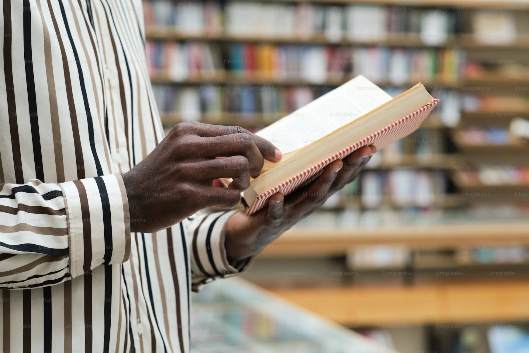 Close-up of an open book held in the hands of someone wearing a striped shirt.