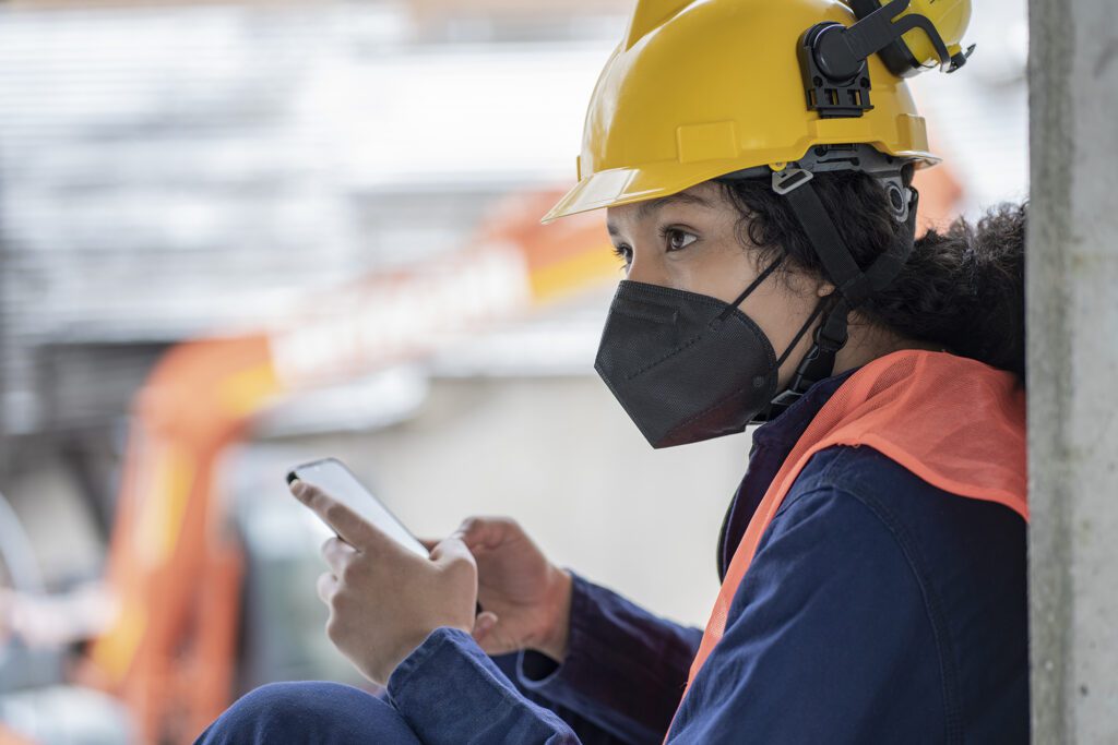 Afro Latino female construction worker is sitting on the ground chatting on her cell phone