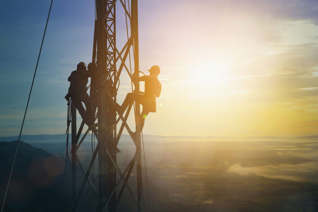 Silhouette electrician work on high ground heavy industry concept. Construction of the extension of high voltage in high voltage stations safely and systematically over blurred natural background.