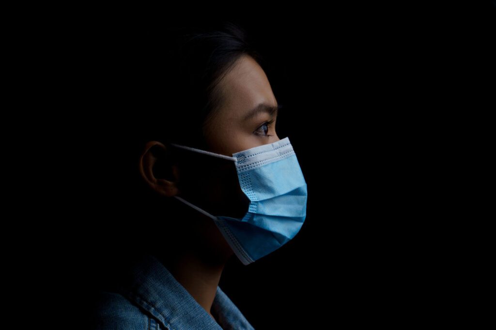 Asian woman wearing protective mask isolated over background. Low key.