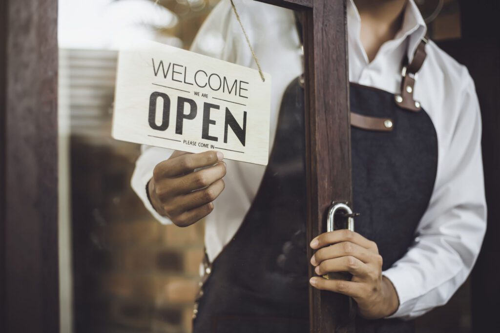 Store owner turning open sign broad through the door glass and ready to service.