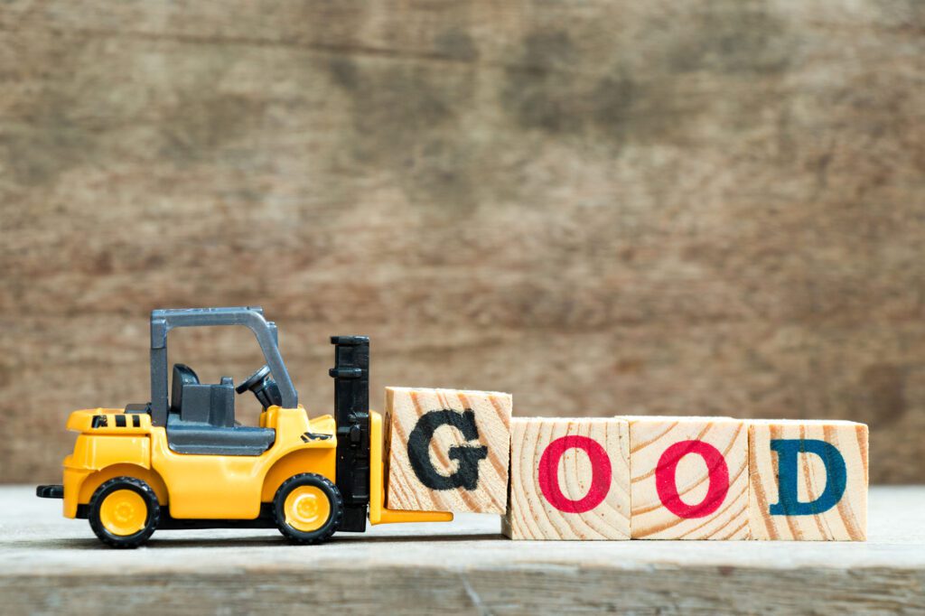 A toy forklift pushing four blocks that spell out the word 'GOOD'.